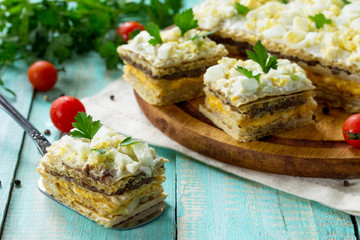 Snack cake on waffle cakes with herring pate, mushroom pate and cheese-egg cream on a kitchen wooden table.