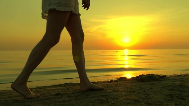 Girl woman is walking along a sandy sea beach barefoot on a sunset background. The girl is walking in slow motion, the sunset is reflected on the sea