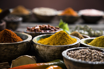 A selection of various colorful spices on a wooden table in bowls