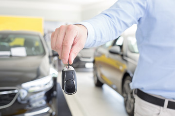 Fototapeta premium male adult dealer hand giving car keys, close-up photo taken indoors, cars at the background