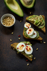 Sandwich avocado with fresh sliced avocado, egg poached and spices on a dark slate or stone background. Copy space. Flat lay, top view.