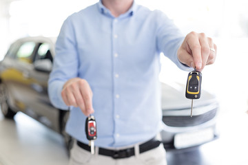 Close up of male adult cardealer holding car keys in each hand, offers a choice of two keys