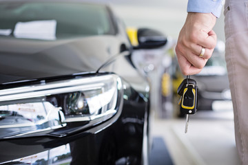 Close up photo of male hand holding a car keys next to a brand new black car indoors in a dealership