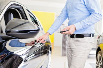Close up photo of male adult person holding a car keys in one hand, opening a car doors with the other hand, keyless door opening