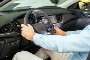 Male adult person sitting inside a new car holding a steering wheel with one hand, tuning radio with the other hand