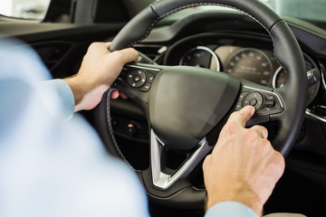 Close up of man sitting in the driver seat, pressing a buttons on steering wheel, view from behind the driver