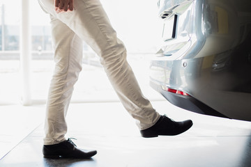 Fototapeta premium close up of male adult person legs opening a car door with leg movement, without having to use the car key, taken indoors in car dealership