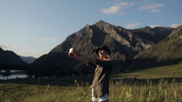 girl traveler takes pictures, makes selfies on the phone among the mountains
