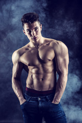 Fototapeta na wymiar Handsome young muscular man shirtless wearing jeans, on dark background in studio shot
