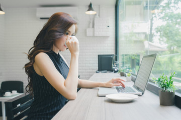 Beautiful young Asian businesswoman drinking coffee and working with laptop in the coffee shop