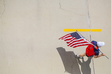 Man walking on cracked cement, carrying an American flag, view from above