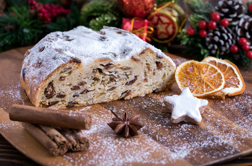 Weihnachtlicher Butterstollen mit Rosinen auf Holztisch mit Gewürzen und Puderzucker