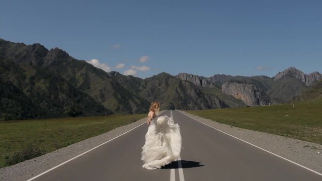 beautiful young woman in a wedding dress running down a mountain road