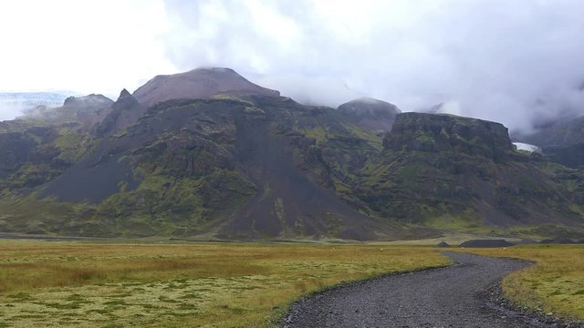Beautiful Icelandic landscape with mountains, dirt road and dramatic  clouds stuck in the mountains. Quick motion
