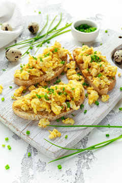 Homemade Quail Scrambled eggs on crispy toast, bread with green onion, chives on white board.