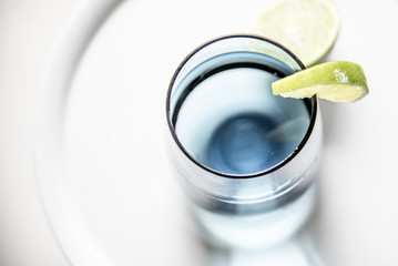 Glass of water with slice of lime, closeup, top view. Water in blue glass with lime macro, white background, horizontal.