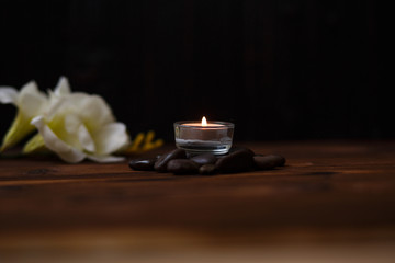 A candle in a glass vase, decoration and various interesting elements on a dark wooden background. Candles burning. Set for spa and massage. stones for massage