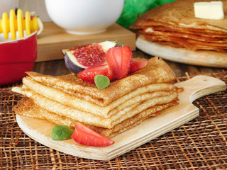A pile of crepes decorated with a strawberry and a fig. Breakfast on a wooden background
