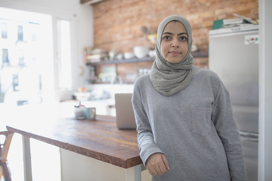 Portrait of businesswoman in hijab leaning on table in kitchen