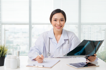 Beautiful asian female doctor examining Xray report in clinic