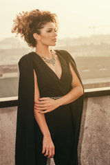 Obraz premium Beautiful and elegant woman standing in the sunlight on rooftop and looking aside