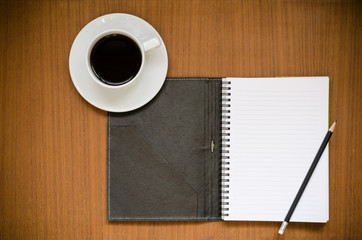 Recycled notebook on blank page white paper with lines and dark cover with black sharp pencil over teak wood background with copy space and black coffee in white cup, office or education concept