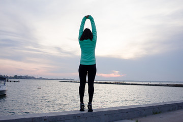 Fototapeta na wymiar young woman do stretching exercises, sunrise in sea background 
