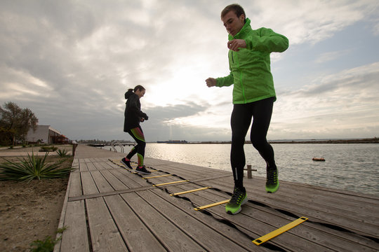 group of young people training outdoors, runners exercises, sea or river background