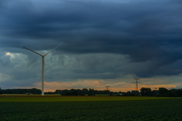 Wind turbines for electrical power generation and power lines in green field on cloudy day in Normandy, France. Renewable energy sources, industrial agriculture concept. Eco friendly energy production