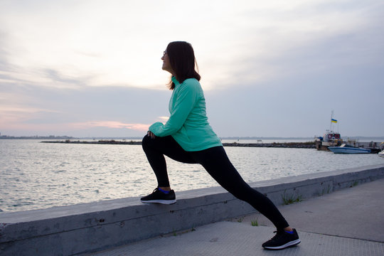 young woman do stretching exercises, sunrise in sea background  