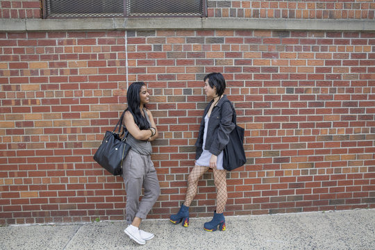 Young women talking beside a brick wall