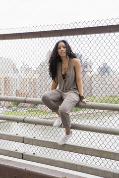 Young woman sitting on a railing on a bridge

