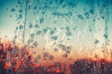 Frosty pattern. Vintage frozen ice texture on the window at sunset. Frozen snowflakes and frost over the sun on frozen Christmas winter background. Colored in blue tone. Instagram filter