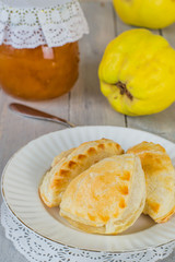   Homemade ruddy pies with a filling, fresh quince fruit and a small glass jar with jam on an old wooden table.