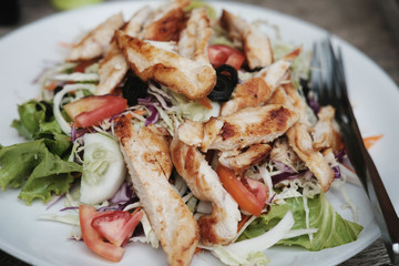 Salad with grilled chicken breast and organic vegetables closeup on white plate on table.