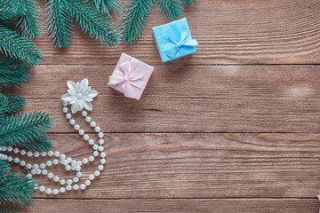 Christmas background. Branches of a Christmas tree, women's necklace and gift boxes on a wooden background with copy space.