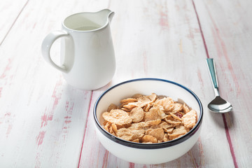 Bowl of cornflakes and milk, with spoon on wooden background, morning sun, ,close-up