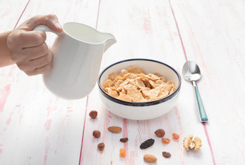 Pouring milk on a bowl of cornflakes  , hazelnut, dry apricot, walnut and nuts on wooden background , top view,  close-up