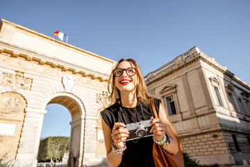 Fototapeta premium Portrait of a young happy woman tourist with photo camera in front of the famous Triumphal Arch during the morning light in Montpellier city, France