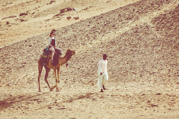 People in the camel caravan going through the sand dunes in the in Aswan desert, Egypt.