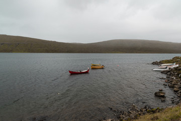 Fototapeta na wymiar one red boat and two yellow boats in a lake on Faroe Islands