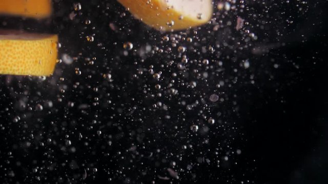Round fresh juicy grapefruit slice plunging into transparent water with explosive stunning splash. Underwater high-speed slow motion shot on black background. Pomelo isolated.