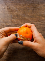 Woman hand peeling ripe sweet tangerine. on a wooden background. with copy space. top view