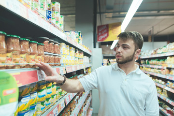 A handsome man makes a choice at the supermarket. A man buys canned food at the store. Shopping in a supermarket.