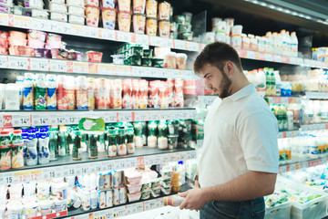 A man chooses yogurt in a supermarket. The buyer selects dairy products. in the shop. A man buys food in a supermarket.