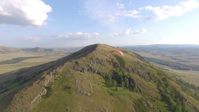 AERIAL: A paraglider flies over a huge rocky mountain and rises higher into the sky. Beautiful view on mountain landscape with smokey horizon.