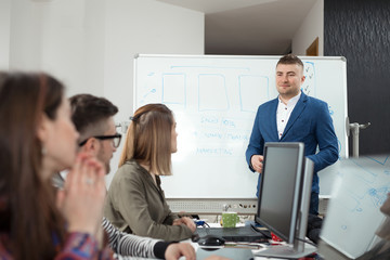 Young businessman presenting new business plan to his coworkers on a meeting in a board room