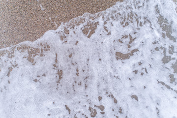 Texture of a sea foam rolling on a sandy beach