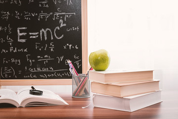 School books with apple on desk over school board background