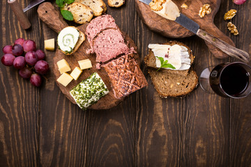 Obraz na płótnie Canvas Assorted cheeses on wooden boards plate, grapes, bread wine and pate on dark wooden background, top view, flat lay, copy space.